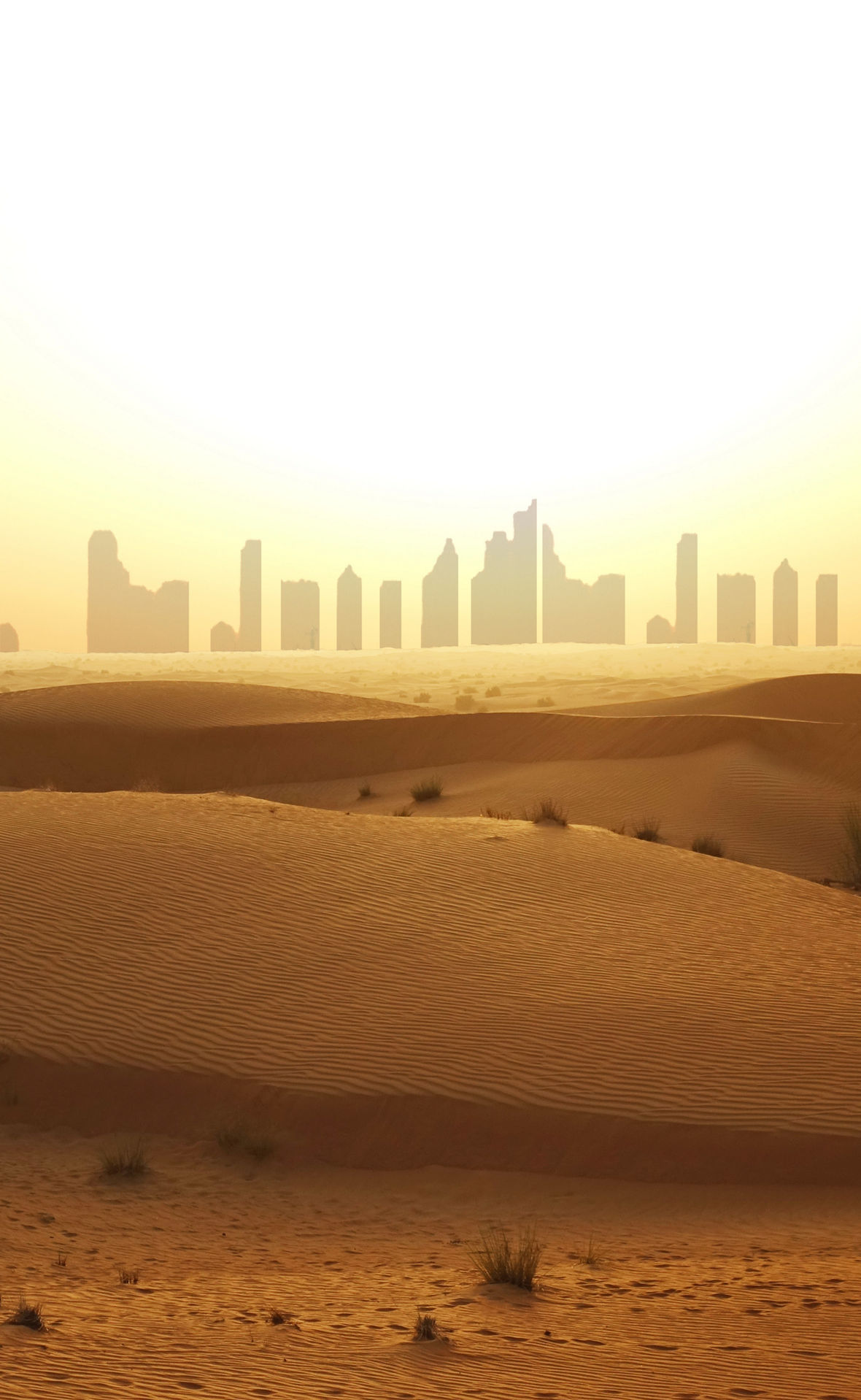 Im Vordergrund Dünen, im Hintergrund als Silouetten die Wolkekratzer von Dubai