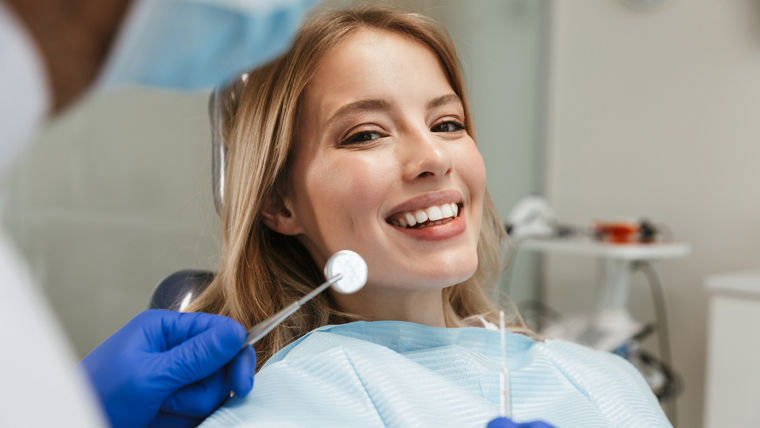 Image of beautiful young woman sitting in dental chair at medical center while professional doctor fixing her teeth