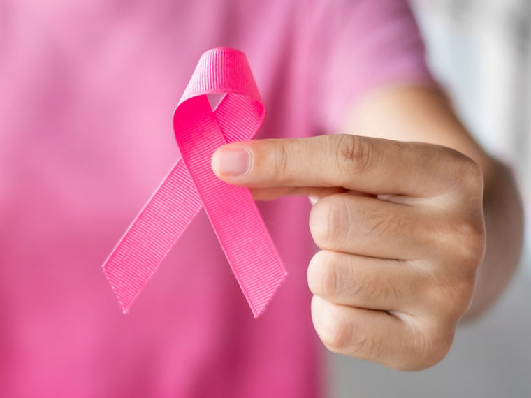 A female hand holds a pink ribbon in remembrance of Breast Cancer Awareness Month in October.