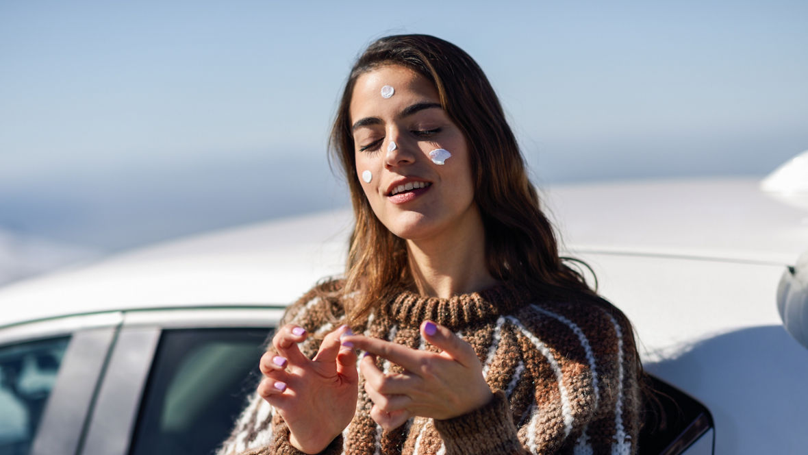 Young woman applying sunscreen on her face in snowy mountains in winter, in Sierra Nevada, Granada, Spain. Female wearing winter clothes.