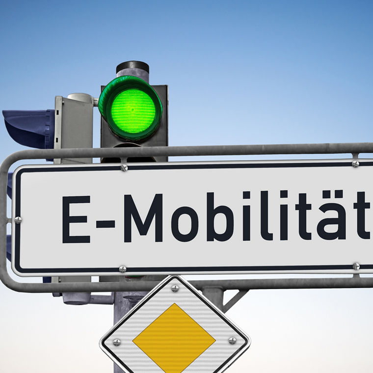 EIn Straßenschild vor einer Ampel, die Grün zeigt, und an dem ein Vorfahrtsschild befestigt ist. Auf dem Schild, das ein Richtungspfeil nach rechts ist, steht: E-Mobilität.