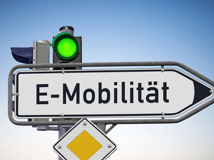 EIn Straßenschild vor einer Ampel, die Grün zeigt, und an dem ein Vorfahrtsschild befestigt ist. Auf dem Schild, das ein Richtungspfeil nach rechts ist, steht: E-Mobilität.