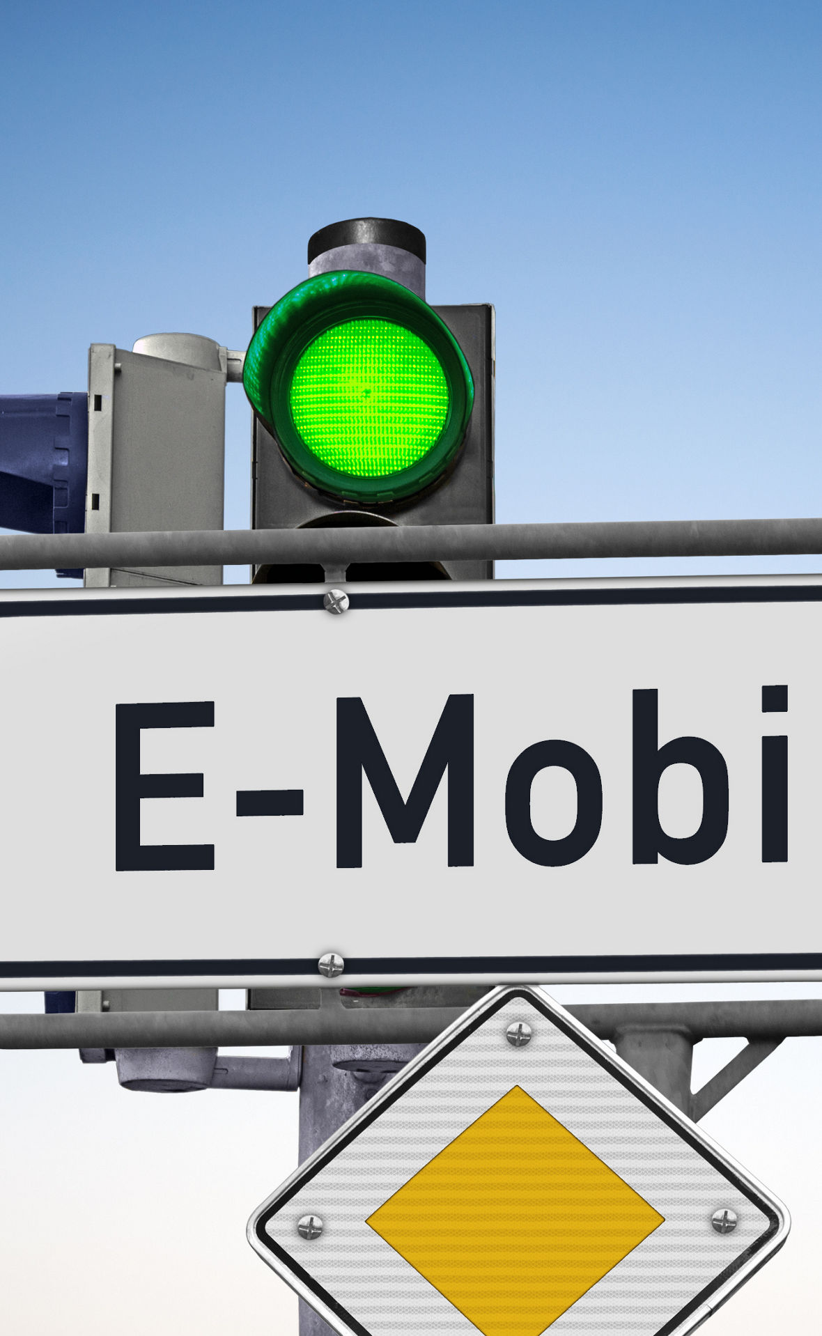 EIn Straßenschild vor einer Ampel, die Grün zeigt, und an dem ein Vorfahrtsschild befestigt ist. Auf dem Schild, das ein Richtungspfeil nach rechts ist, steht: E-Mobilität.