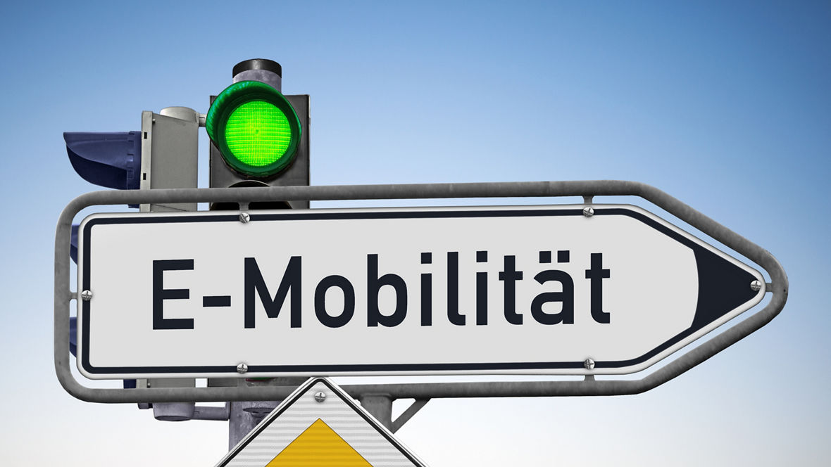 EIn Straßenschild vor einer Ampel, die Grün zeigt, und an dem ein Vorfahrtsschild befestigt ist. Auf dem Schild, das ein Richtungspfeil nach rechts ist, steht: E-Mobilität.