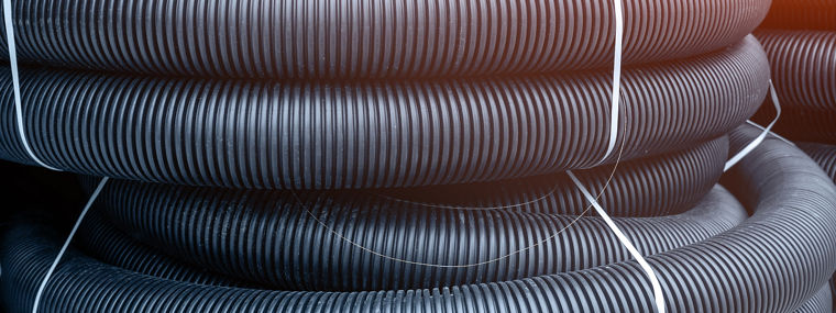 Many rolled colis of new black corrugated goffred plastic electric plumbing drainage pipe prepared for installation near building construction site. Drain sewage tube hose conduit pipeline
