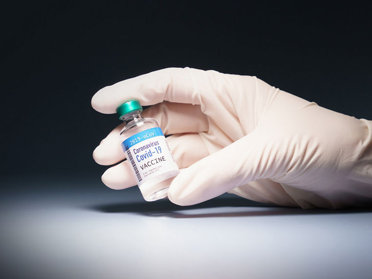 Hand of a researcher holding an ampoule with coronavirus, SARS-CoV-2, in spotlight.
