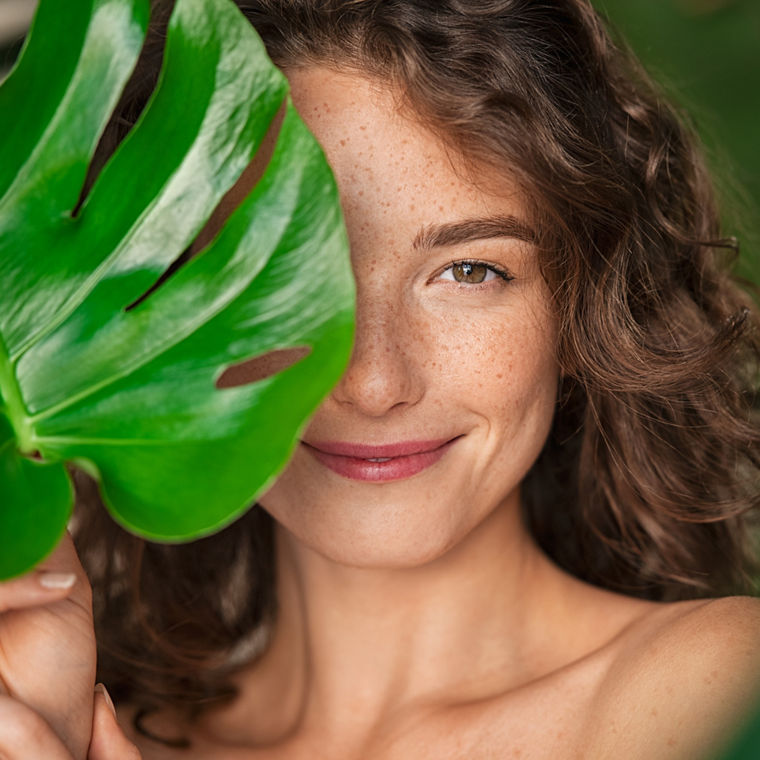 Portrait einer Frau, ihr Gesicht teilweise von einem grünem Blatt bedeckt.