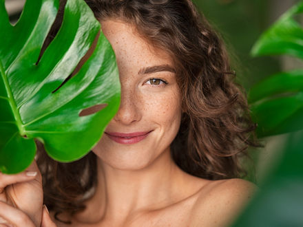 Portrait einer Frau, ihr Gesicht teilweise von einem grünem Blatt bedeckt.