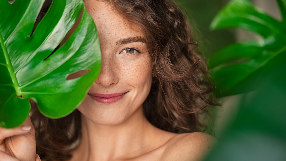 Portrait einer Frau, ihr Gesicht teilweise von einem grünem Blatt bedeckt.
