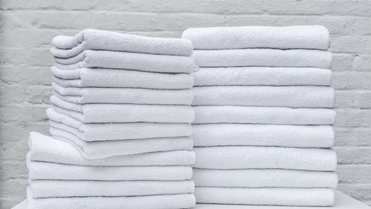 A lot of white towels on the white table in laundry or hotel on white background.