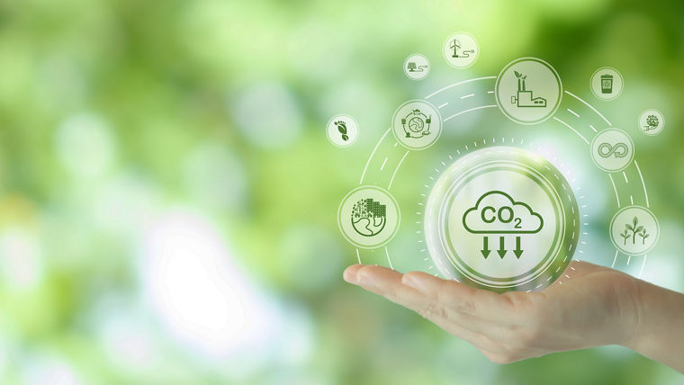 A hand holding a circular icon representing CO2 reduction, surrounded by various green icons symbolizing sustainability, renewable energy, and eco-friendly practices, set against a blurred green background. This image emphasizes the importance of innovative solutions for combating climate change.