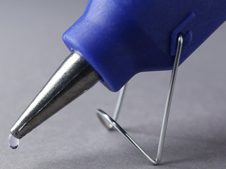 Ein Tropfen Klbstoff häng an der Spitze einer Klebepistole