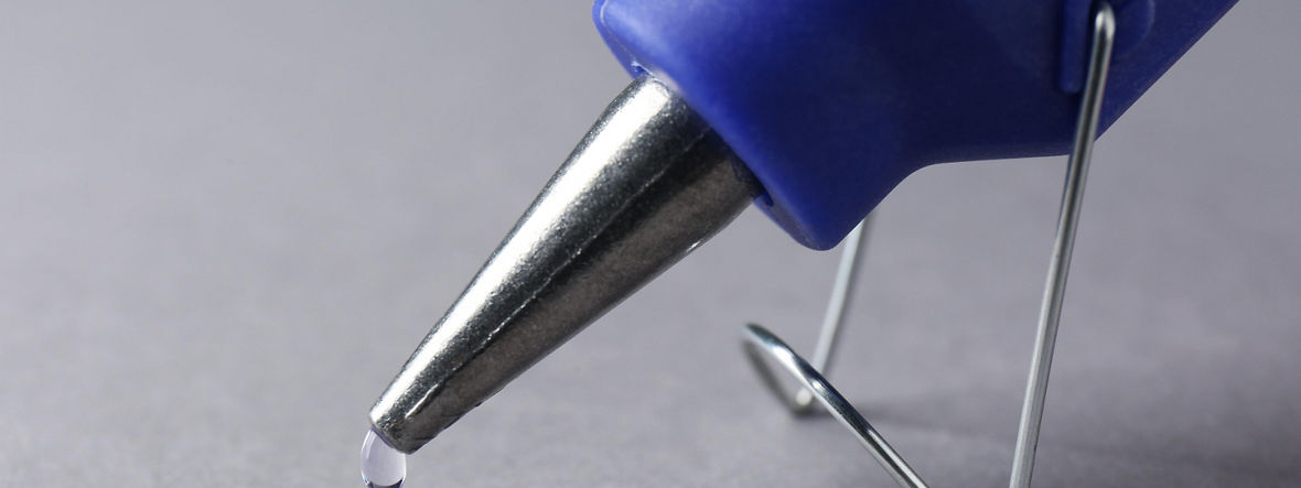 Ein Tropfen Klbstoff häng an der Spitze einer Klebepistole