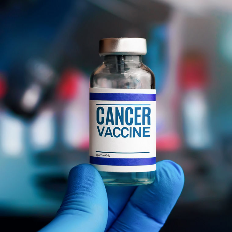 A gloved hand holds up an ampoule labeled “cancer vaccine”
