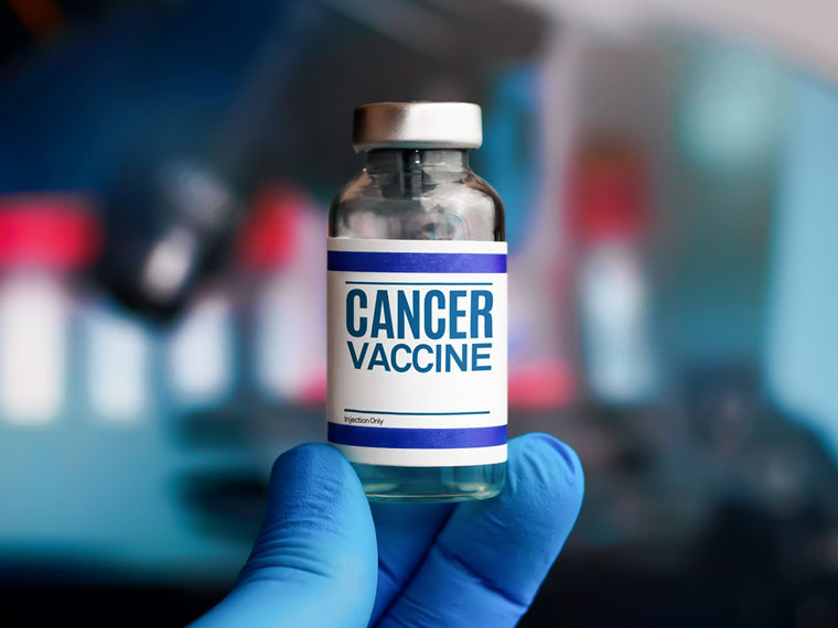 A gloved hand holds up an ampoule labeled “cancer vaccine”