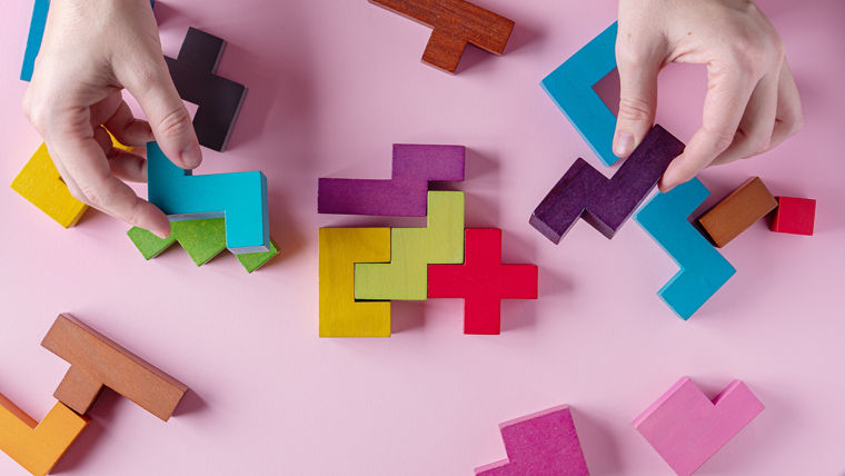 Different colorful shapes wooden blocks on pink background, flat lay, copy space. Geometric shapes in different colors, top view. Abstract Background. The concept of logical thinking.