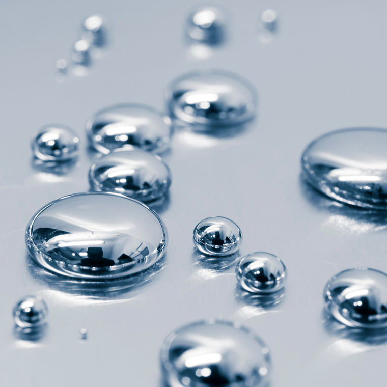 A good twenty droplets of mercury on a gray surface.