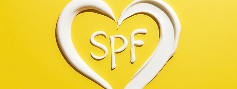 SPF word shaped like heart made of sunscreen cream on yellow background. SPF cream for safe sunbathing and sun protection