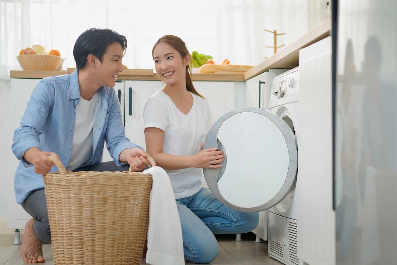 A young couple kneeling in front of a washing machine and filling it together. Fabric softeners are in high demand on the Asian market.