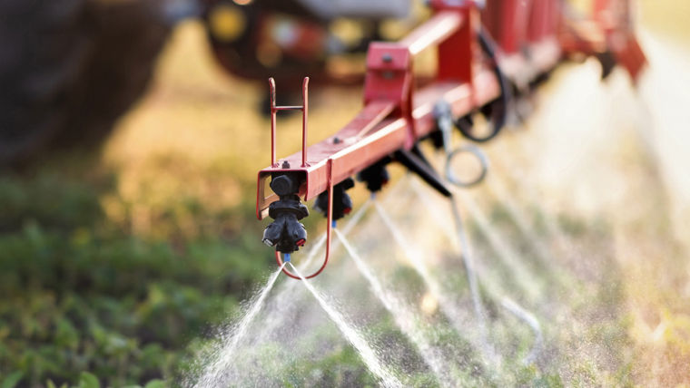 Sprayer nozzles on tractor boom spraying plant care over young crop plants