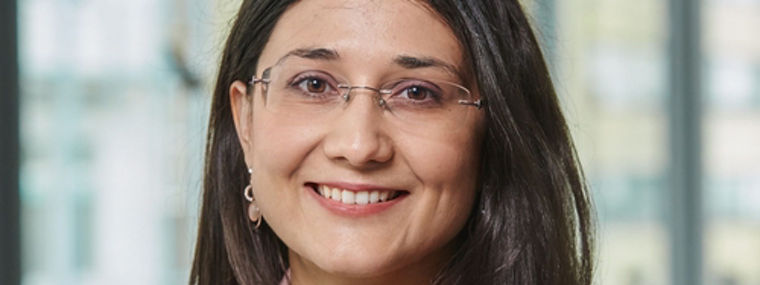 A woman in a pink blazer stands confidently in a modern office environment.
