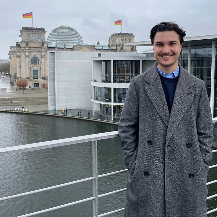 A person stands on a balcony overlooking the Reichstag building and the Spree River in Berlin, Germany.