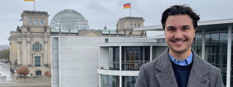 Eine Person steht am Wasser mit Blick auf das Reichstagsgebäude und moderne Architektur im Hintergrund.
