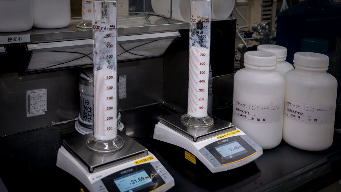 A measuring cylinder with white powder is placed on each of two electronic scales. Three small containers can be seen next to it.