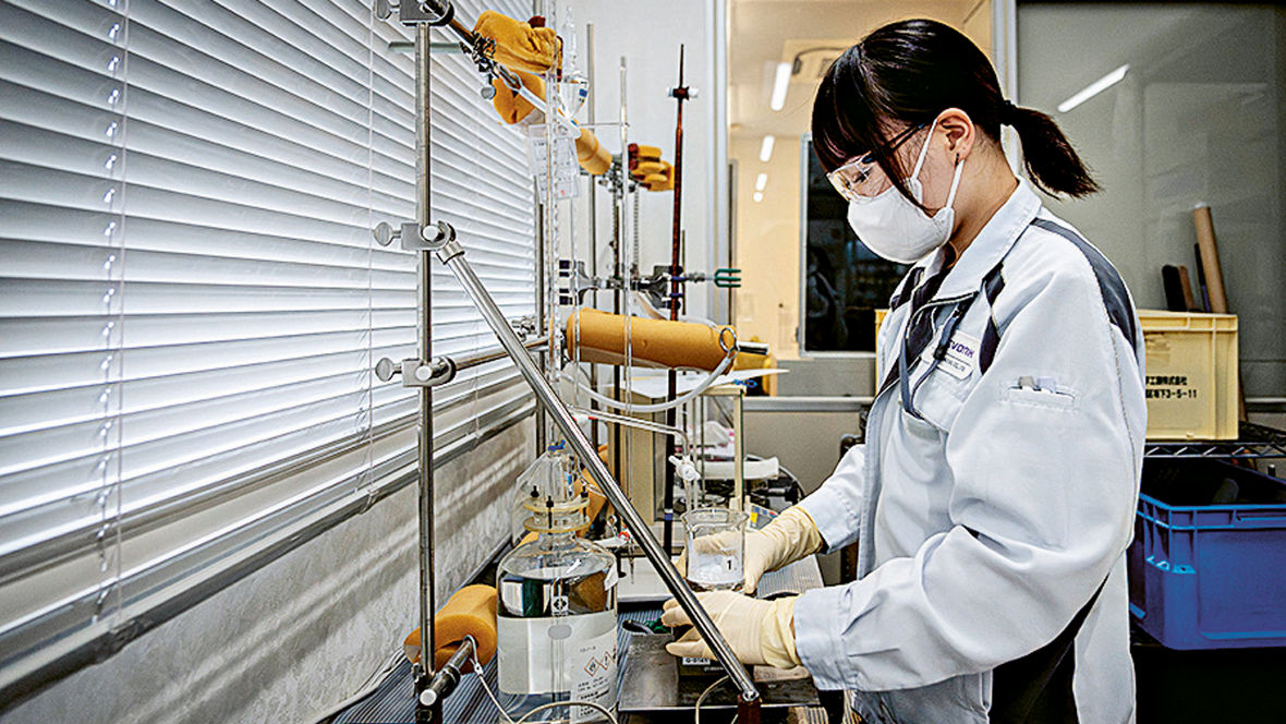 An employee of the AEROXIDE® plant stands at a laboratory bench wearing a face mask and checks a product sample.
