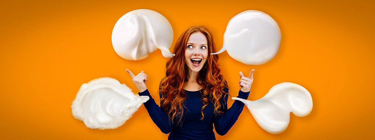 Excited young redhead woman pointing upwards towards blank copy space on a white wall with both hands and an animated expression