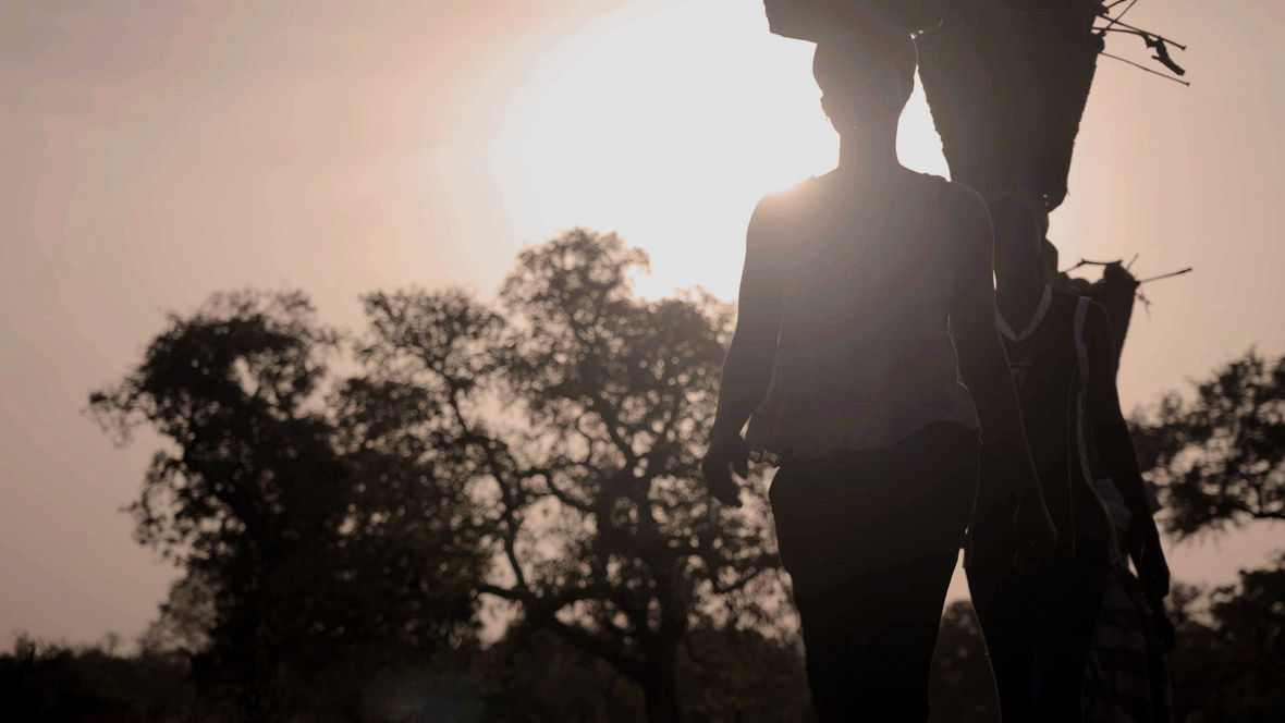 Zwei Frauen mit Körben auf dem Kopf im Sonnenuntergang, dahinter ein Affenbrotbaum.