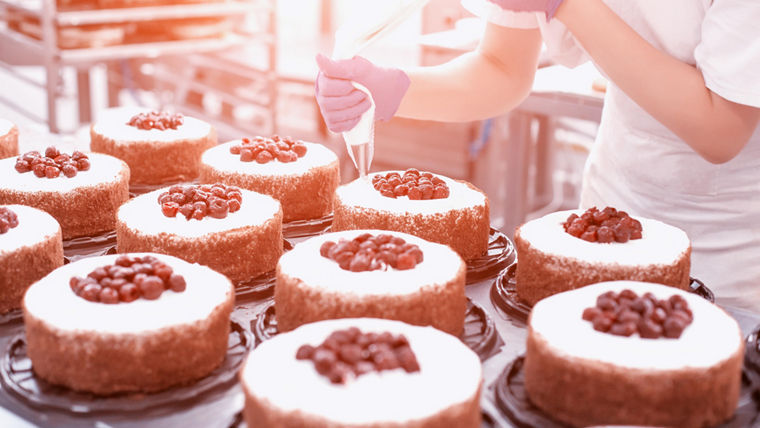 Pastry chef girl makes a cake from fresh biscuit berries and cream. Mass production of cakes and sweets, confectionery factory