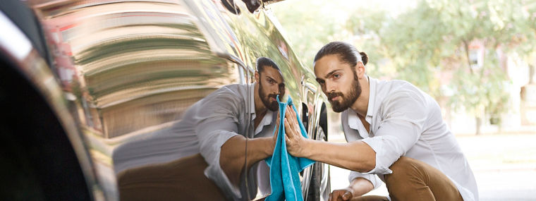Junger Mann reinigt Seite eines Autos zeigt seine Reflexion