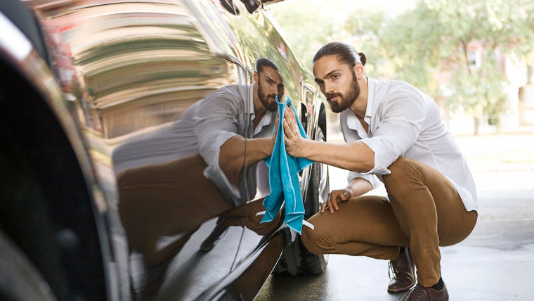 Junger Mann reinigt Seite eines Autos zeigt seine Reflexion