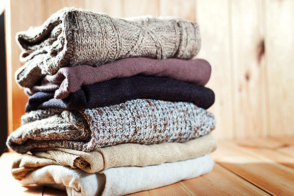 Pile of knitted winter clothes on wooden background, sweaters, space for text, selective focus