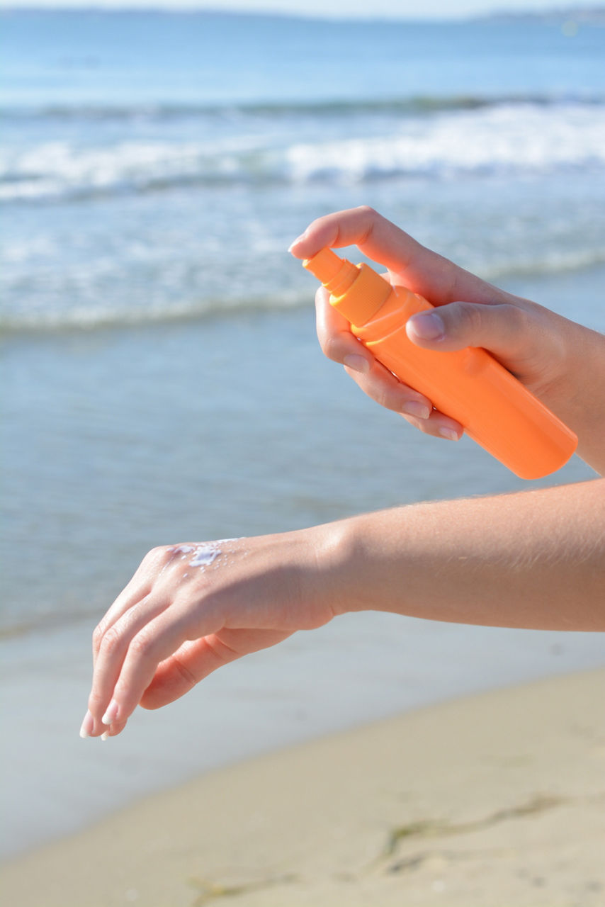 Woman applying sun protection cream on her hand at beach, closeup