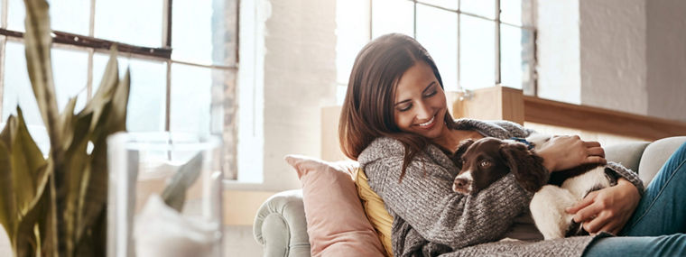 Smile, dog and woman on a couch, relax and love with joy, playful and carefree at home. Female person, girl and lady on a sofa, pet and happiness on a sofa, freedom and break with a domestic animal