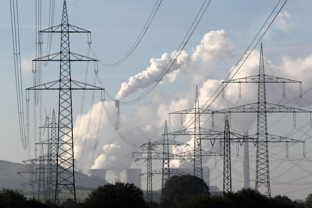 Hochspannungsleitungen vor den Kühltürmen eines Kraftwerks. Daneben ein Windrad.