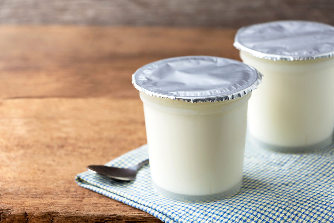 A breakfast of yogurt with a spoon placed on a wooden table. Yogurt made from milk fermented by added bacteria, often sweetened and flavored.