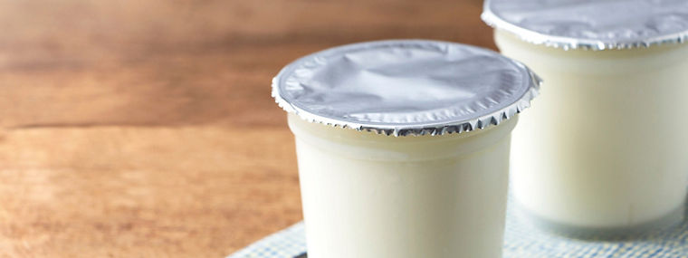 A breakfast of yogurt with a spoon placed on a wooden table. Yogurt made from milk fermented by added bacteria, often sweetened and flavored.
