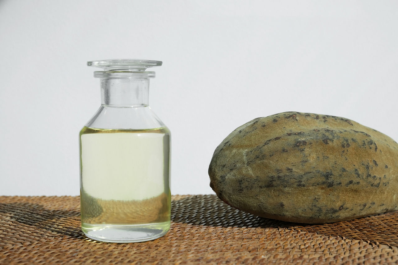 A baobab fruit lies next to a glass bottle with a light, transparent oil.