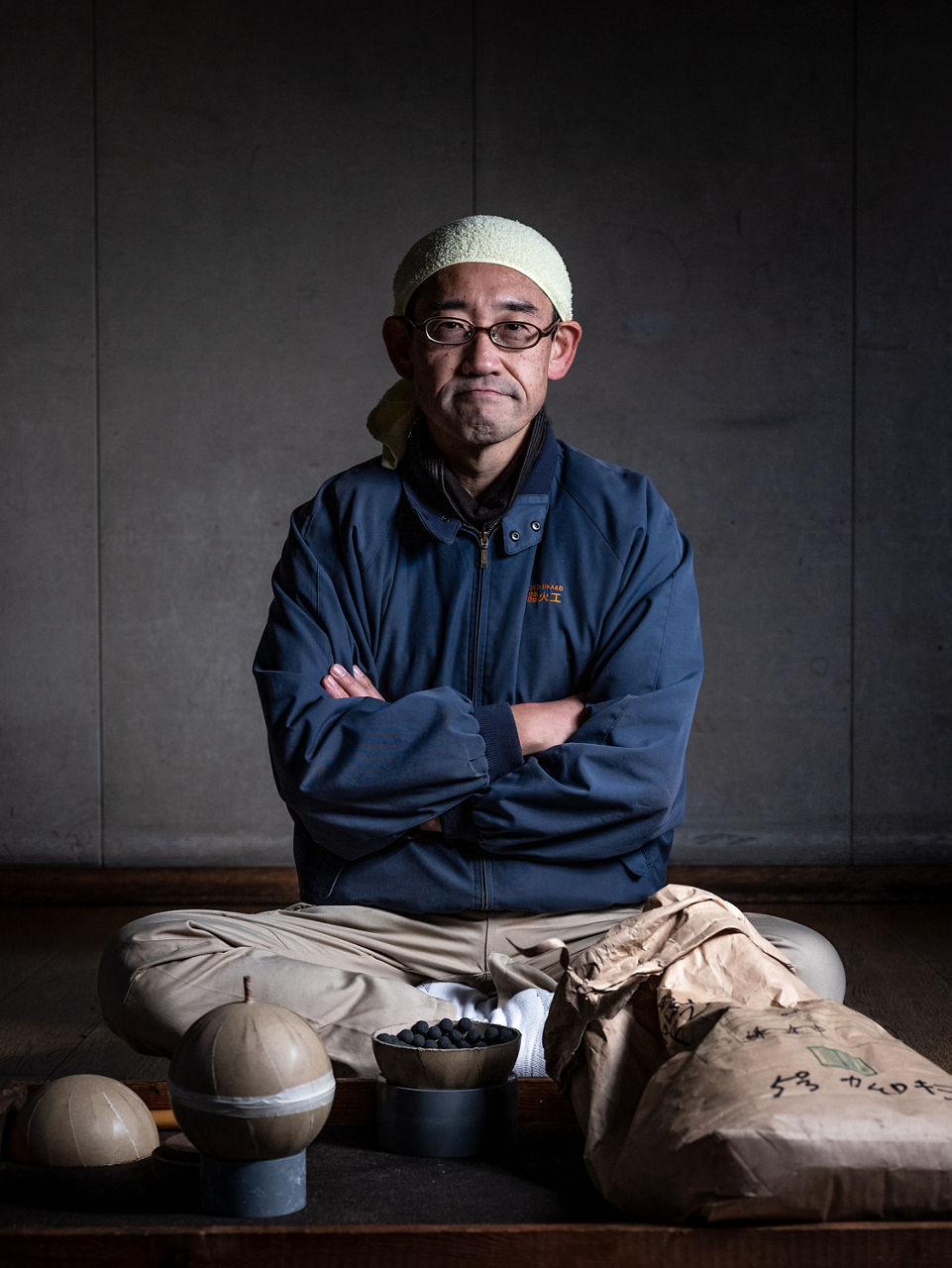 Hideki Kubota sits on the ground between pots of material and some pyrotechnic balls.