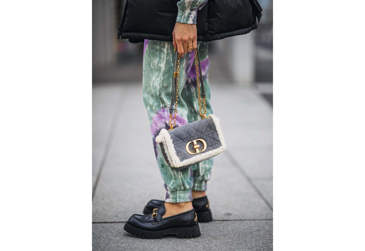 Frauenbeine mit Lederschuhen mit Schnallen und eine Handtasche mit den Initialien "CD".