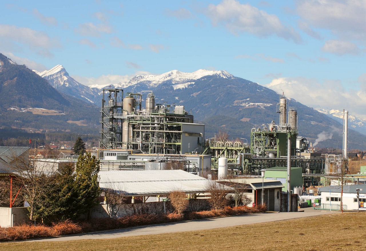 Blick auf das Evonik-Werk in Weißenstein, im Hintergrund die Alpen mit einigen schneebedeckten Gipfeln.