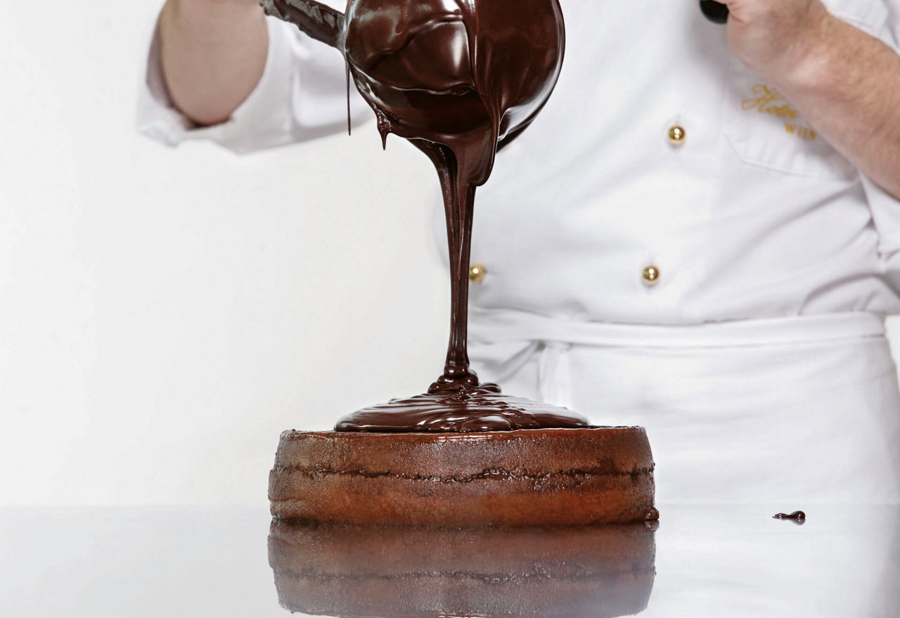 Ein Konditor lässt flüssige Schokolade auf einen Tortenboden fließen.