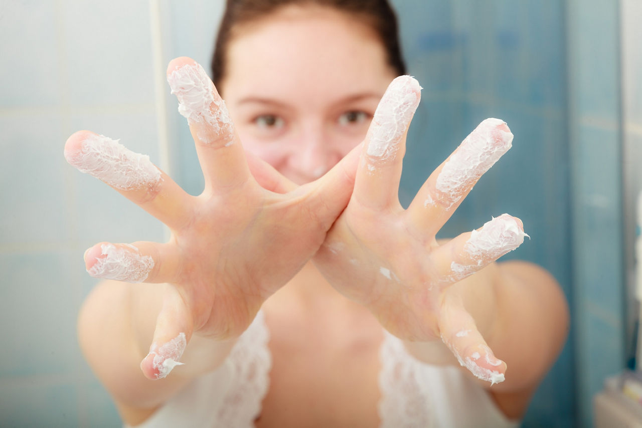 Young woman with cleansing moisturizing skin cream on face. Girl taking care of dry complexion layering moisturizer. 