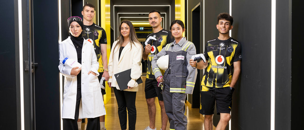 Six people stand in a modern hallway with illuminated yellow and white rectangular frames.