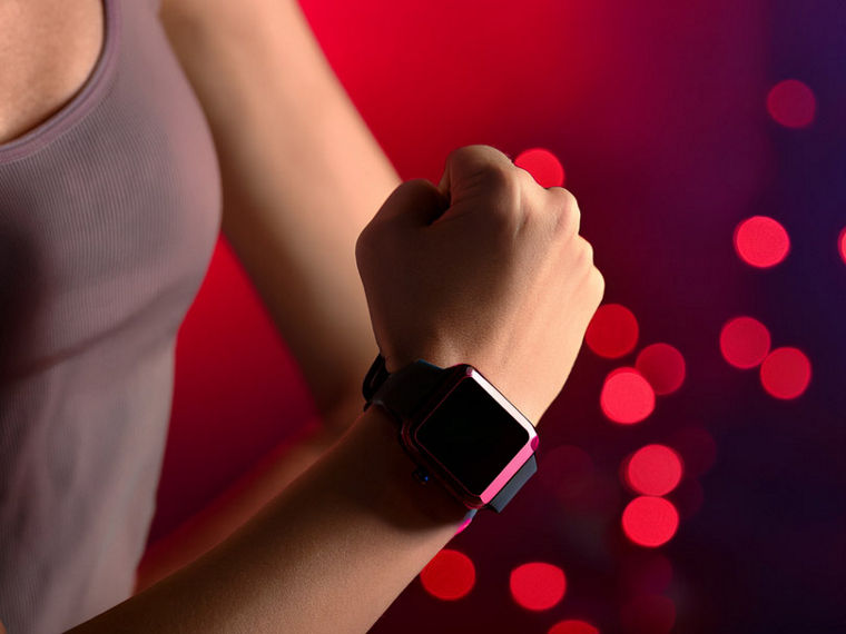 The right forearm of a female athlete wearing a smartwatch against a reddish background.