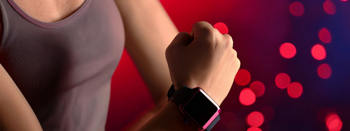 Der rechte Unterarm einer Sportlerin mit einer Smartwatch for rötlichem Hintergrund.