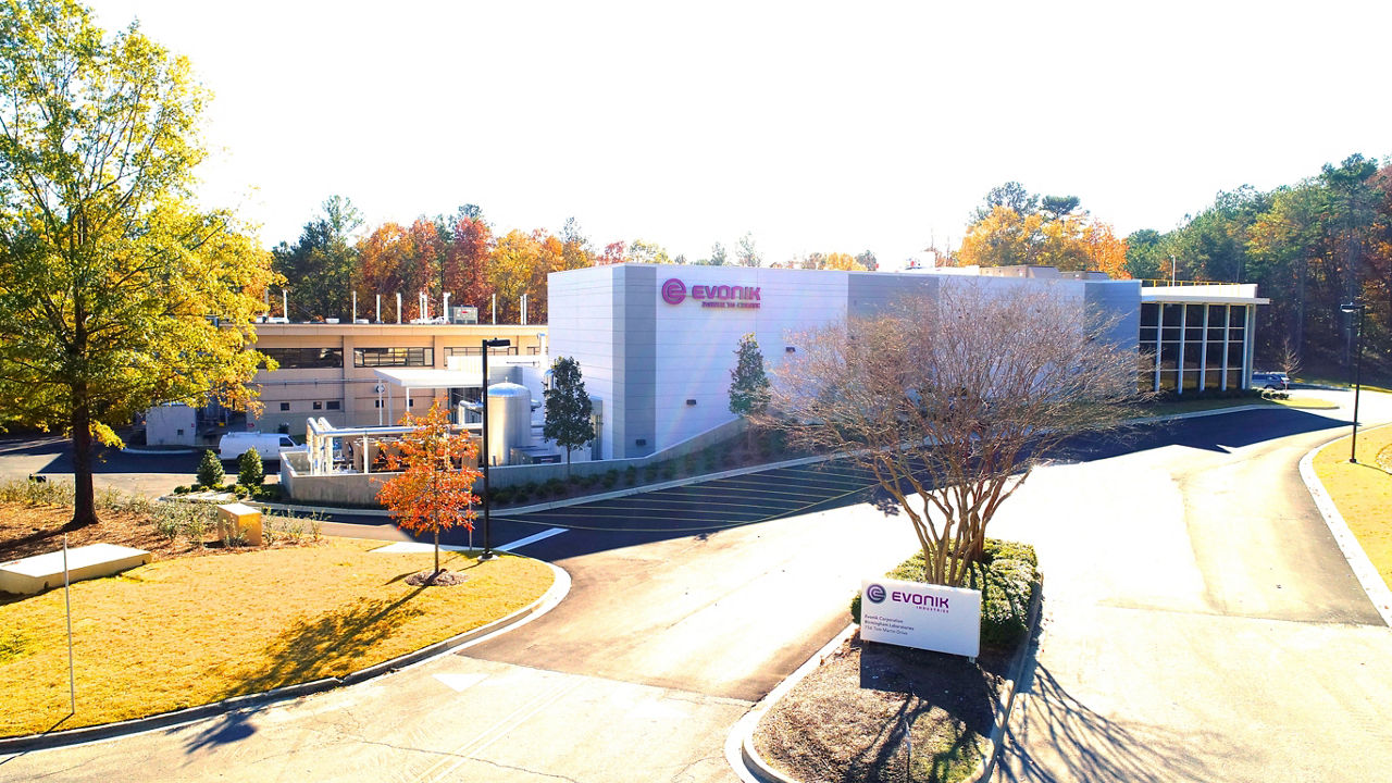 An exterior view of the angular building with the Evonik logo. Trees surround the structure, and a wide driveway leads up to it.